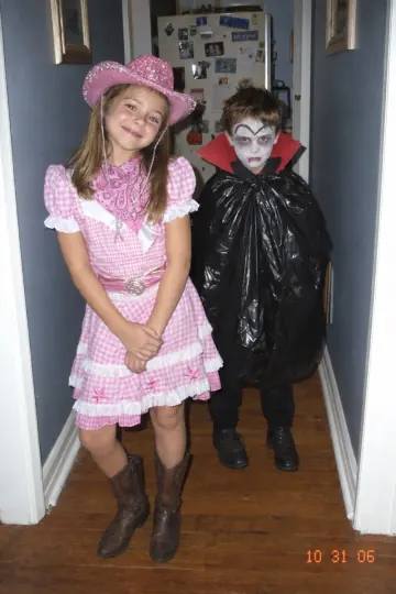 A girl in a pink cowgirl costume next to a boy in a trash bag vampire costume